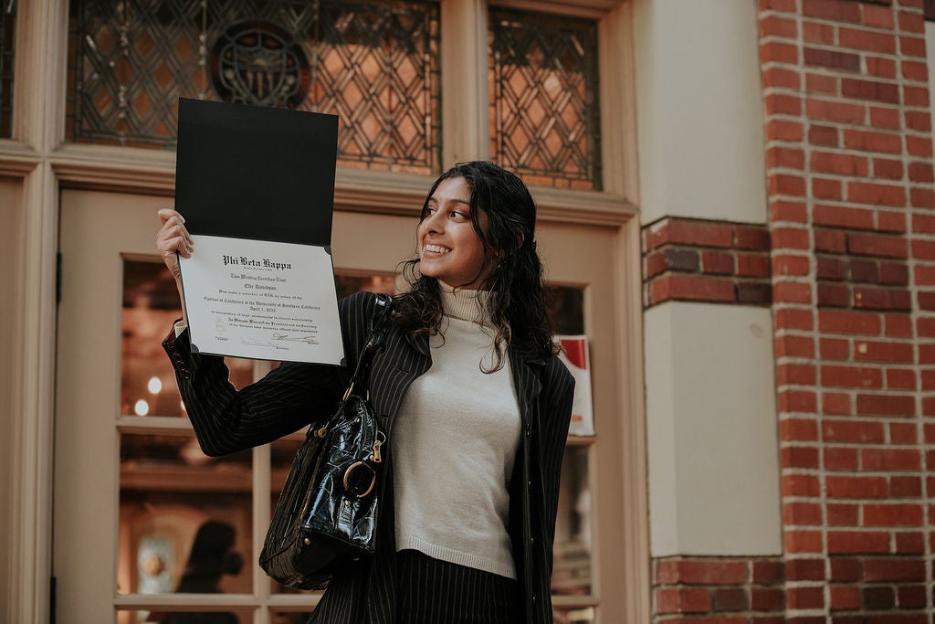 Inductee holding membership certificate up at right shoulder, and looking at it with an expression of pride and joy.