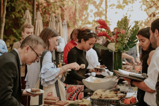 Inductees and guests serving themselves at outdoor buffet. In the background are florals and a row of closed taupe umbrellas.