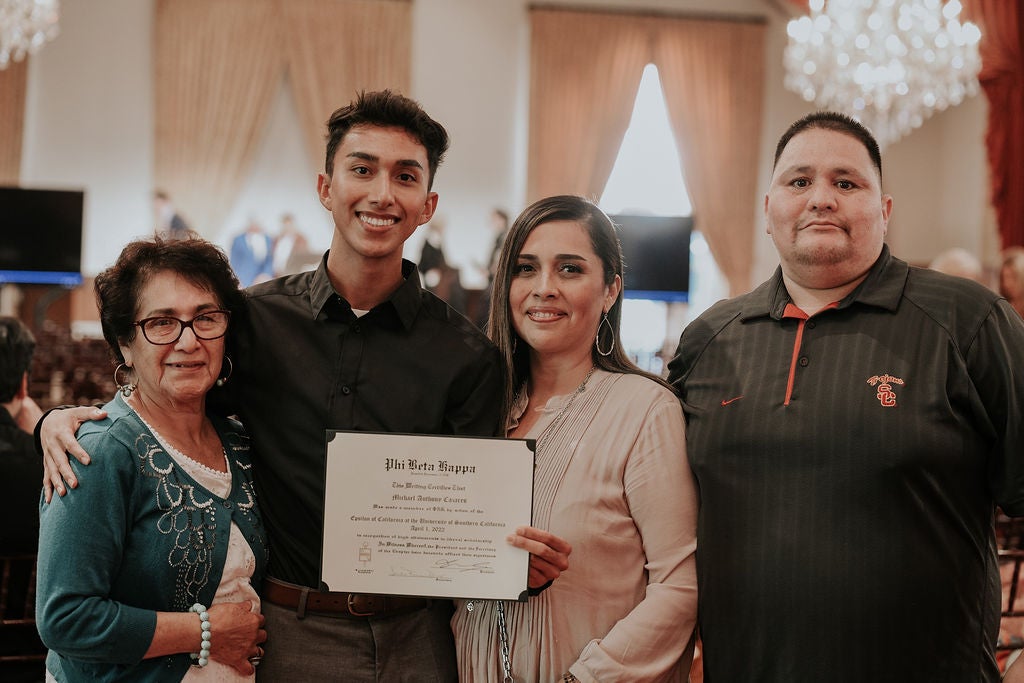 Inductee smiling and holding membership certificate, standing in Town and Gown with three guests.