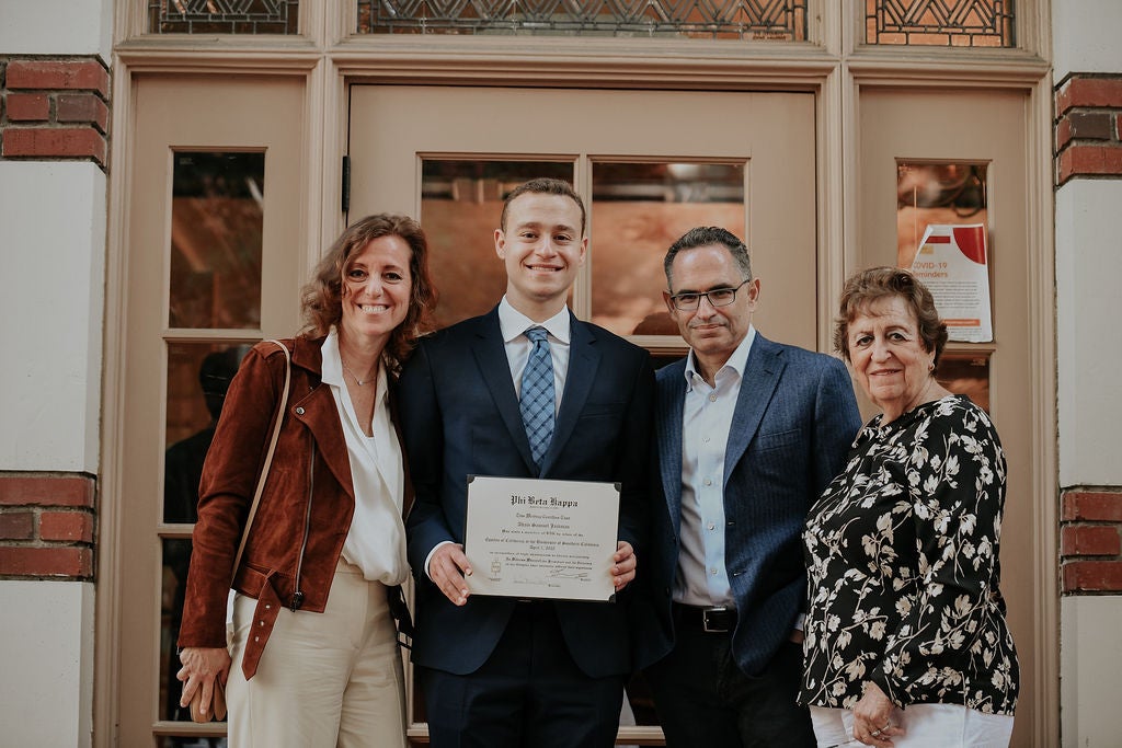 Inductee holding membership certificate, smiling and standing at doorway with three guests.
