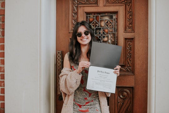 Inductee holding membership certificate, smiling and standing at doorway.
