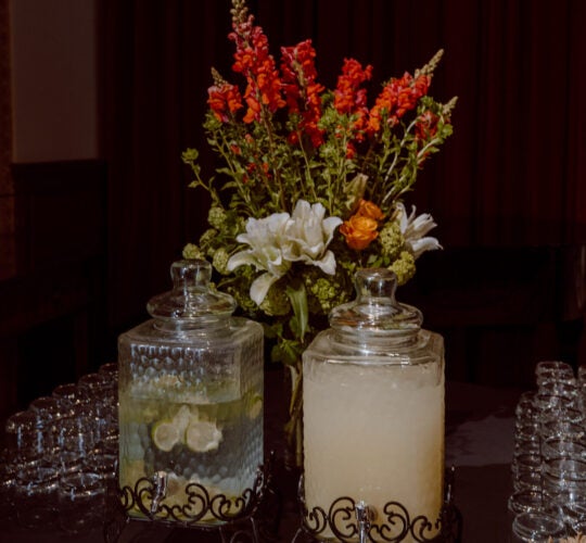 Glass canisters of water and lemonade on beverage table with dried florals.