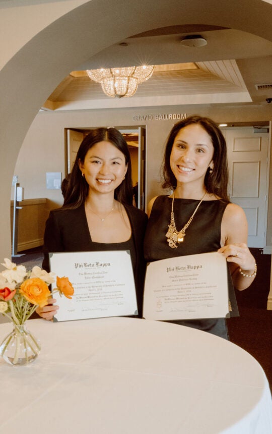 Two inductees standing at table, smiling while holding membership certificates