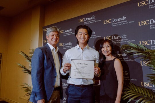 Inductee smiling while holding membership certificate. Standing with two guests.