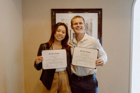 Two inductees standing and smiling while holding membership certificates.
