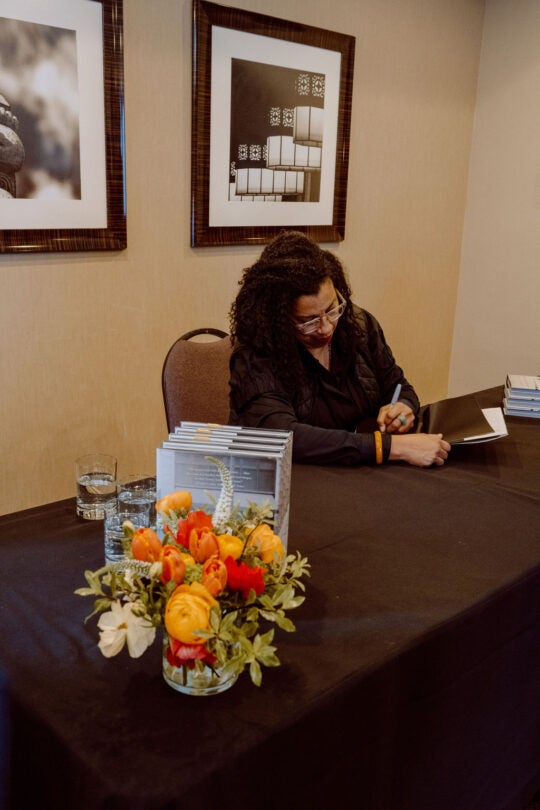 Keynote speaker Robin Coste Lewis signing books at table. Florals in foreground.