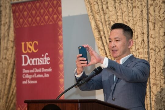 Keynote Speaker Viet Nguyen at podium, taking a photo of the audience.