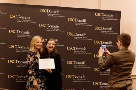 Inductee holding certificate, standing with guest.