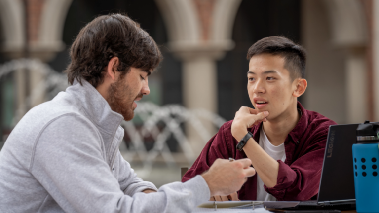 Two male students conversing and working on academic work