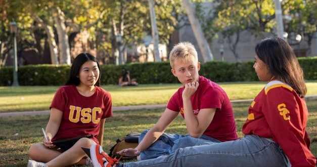 Three students in USC apparel sitting on a grass lawn.