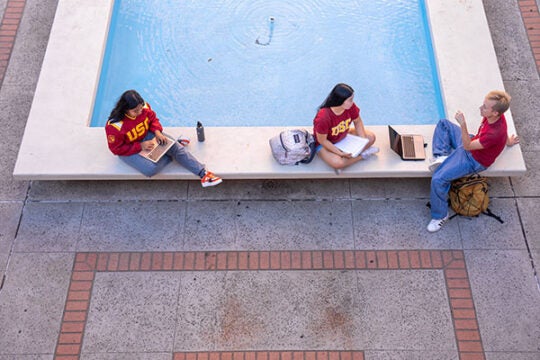Three students study around outside next to a fountain on campus.