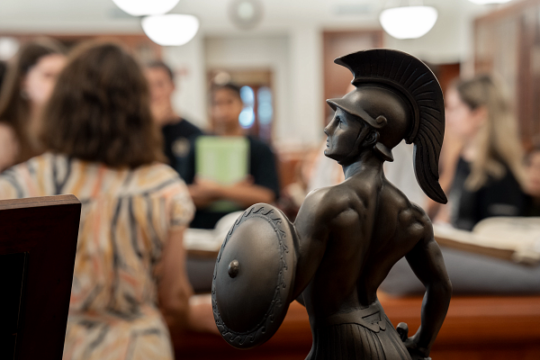 Students meet for class in the USC Special Collections. A small statue of Tommy Trojan is in the foreground of the photograph.