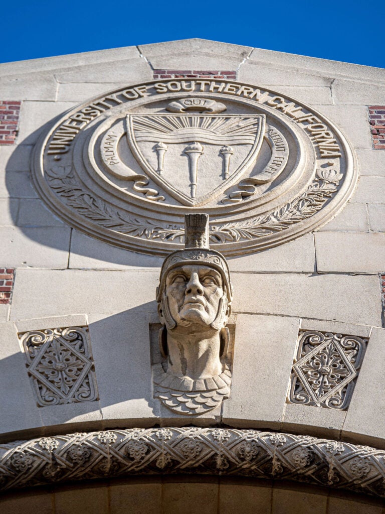 Facade of the Hancock Foundation Building with a sculpture of the head of Tommy Trojan and the USC seal.