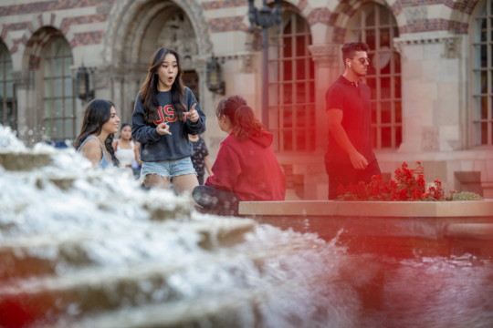 Students sit outside talking next to a fountain on campus.