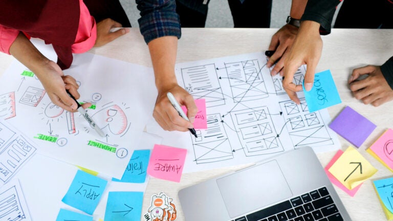 top down image of table with sticky notes and drawings depicting how to test user experience with hands interacting with items on table