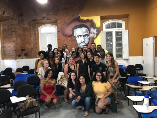 A group of students pose for a picture in front of mural depicting shape of African continent and a portrait of activist Steve Biko