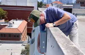 Prof. William Berelson installs a USC Carbon Census senso on a roof with L.A.'s skyline in the background