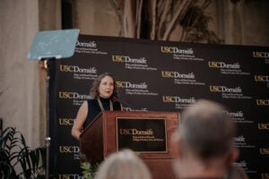 Dean Amber Miller speaks from a lectern in front of a USC Dornsife banner to an audience