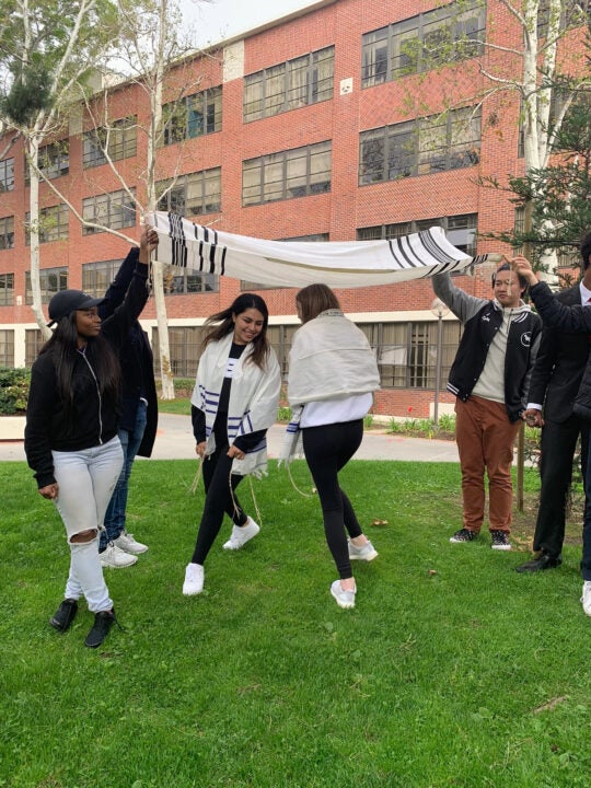 Students dance on lawn wearing Jewish prayer shawls