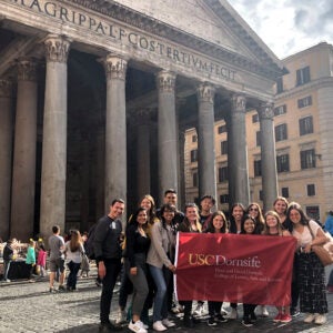 group of students with usc dornsife flag in Italy in front of pantheon
