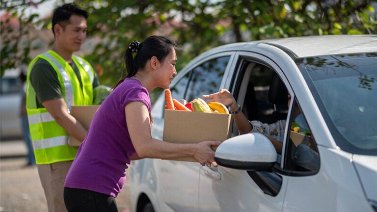 Woman delivers box of produce to person parked in a car.