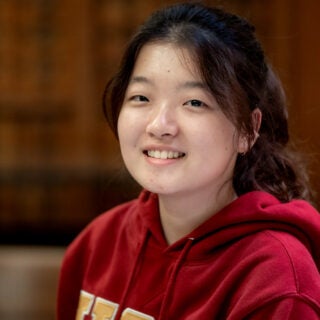 Portrait of Student Nicole N. wearing a red hoodie with library in the background