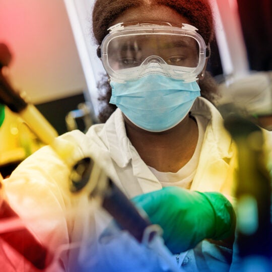 student with mask and safety glasses on using pipette in lab coat