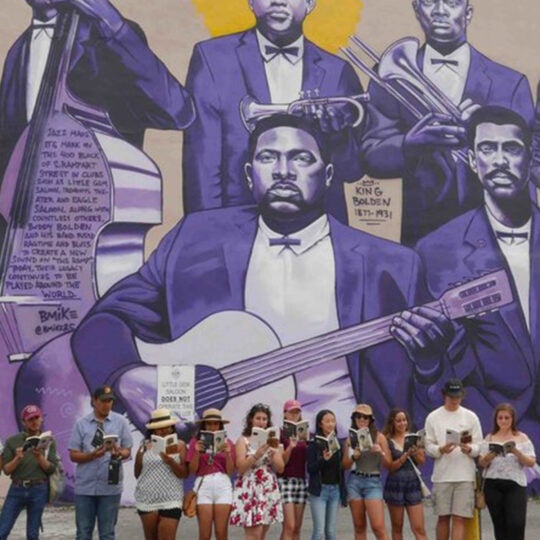 group of students in new orleans reading under big mural of jazz musicians painted in purple