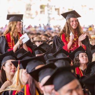 Two graduates in regalia stand and clap during the 2023 USC Dornsife Commencement ceremony.