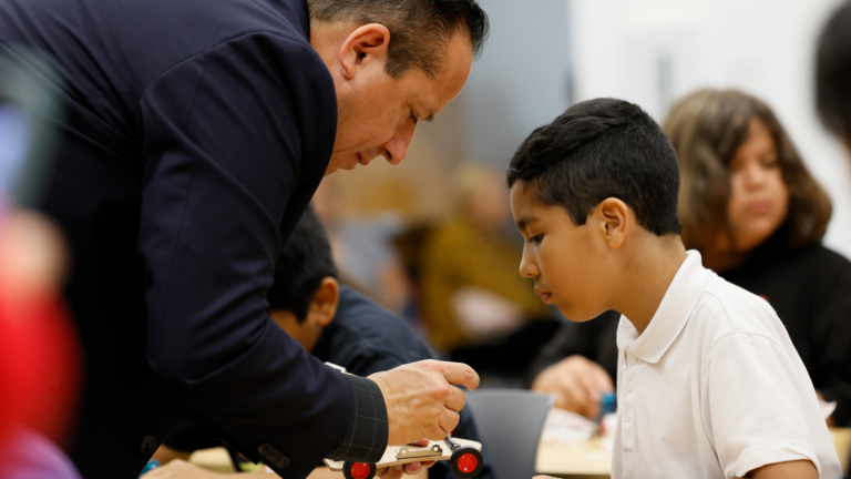 A man in a suit and a young boy working on building a model car together.
