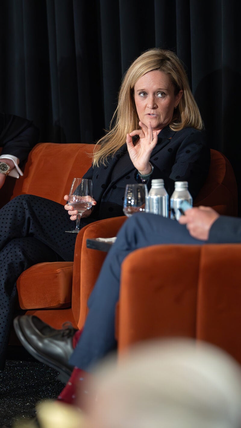 A woman with blonde hair in a suit (the comedian Samantha Bee) gesticulating as she speaks on a panel on a stage with brown chairs