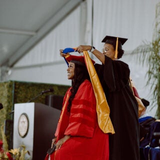 A PhD candidate received her hood from a professor onstage at the 2024 USC Dornsife PhD Hooding ceremony.
