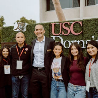 Dean Moh El-Naggar poses with a group of Dornsife students in front of a USC Dornsife sign