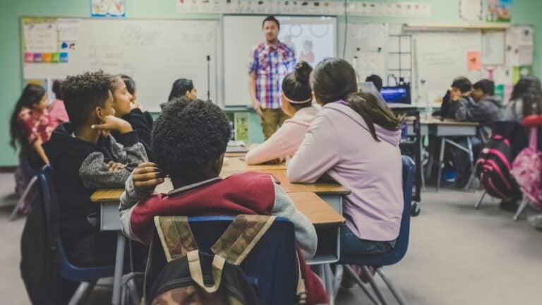 A group of students in a classroom with a teacher at the front of the room