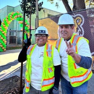 Two people in neon safety vests give peace sign in front of trees