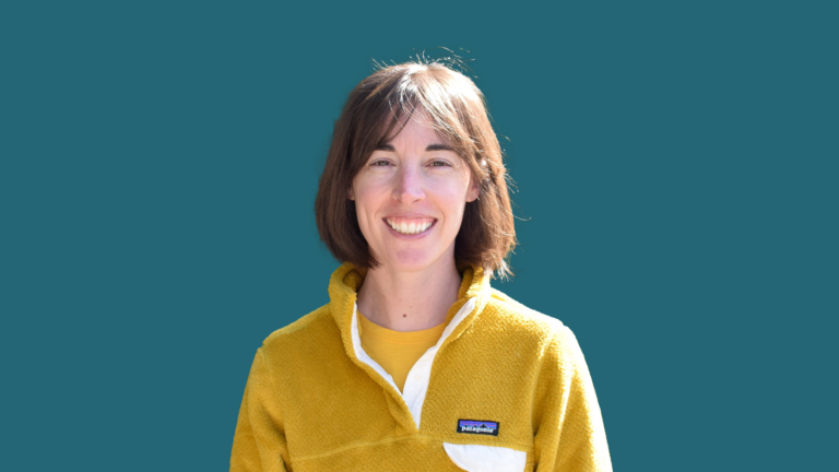 Julia Schwartzman smiles while wearing a yellow fleece jacket against a blue-green background