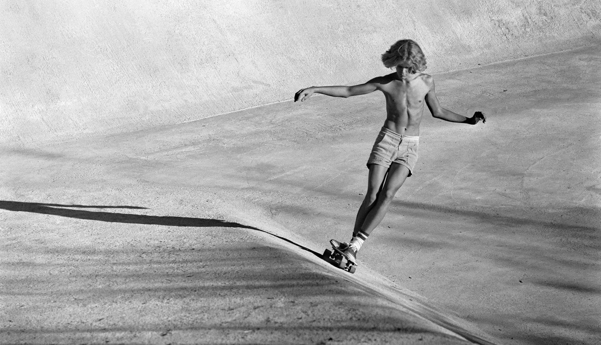 Historical black and white photo of a young man skateboarding.