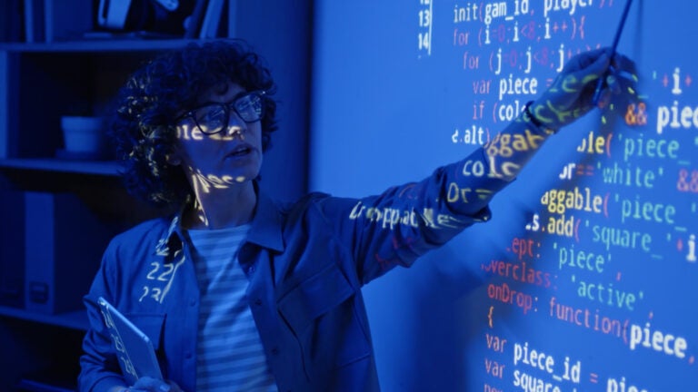 Woman professor pointing at screen with projector casting on the wall and on her