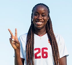 Simi Awugo smiles and makes the Fight On sign wearing a white USC soccer jersey with the number 22 on the chest and a gold necklace.