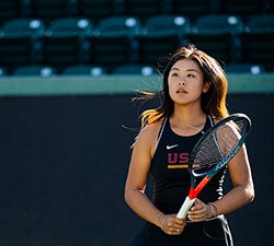 Gabriel Lee stands ready on the tennis court with her racket and wearing a black USC tennis tank top.