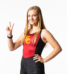 Anika Christensen smiles and makes the Fight On sign while wearing a black and red USC rowing uniform.