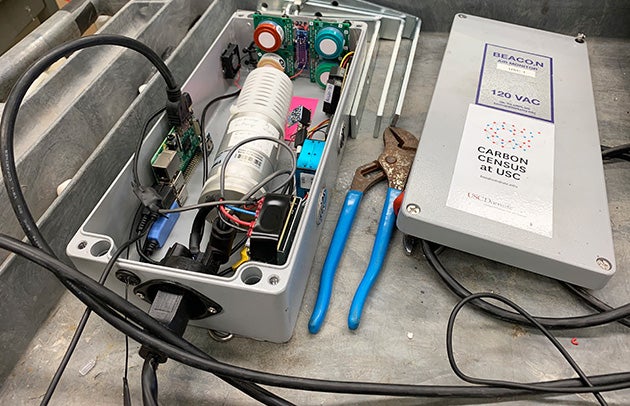 An open sensor box with a tangle of wires and computer components along with a pair of pliers sits on a work cart