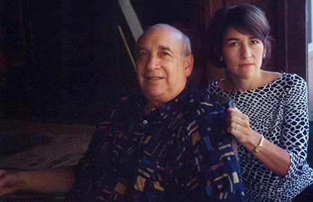 Man in patterned top sits next to woman, she is holding his shoulder.