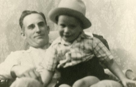 Man seated in chair with boy, wearing a hat, on his lap.