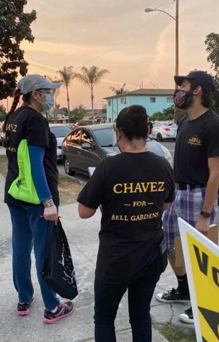 Photo of three people standing on sidewalks. One person wears a shirt that says "Chavez for Bell Gardens"