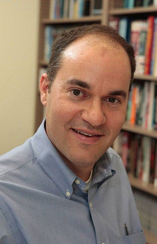 Phot of Matt Kahn in a blue Oxford shirt with book shelves in the background