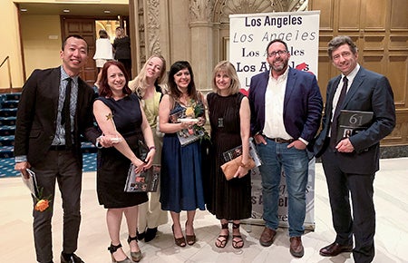 Seven USC Dornsife Office of Communication staff members stand as a group in front of a Los Angeles Press Club banner holding 61st annual Southern California Journalism Awards programs.