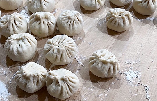 Uncooked baozi rest on a cutting board with flour sprinkled around them