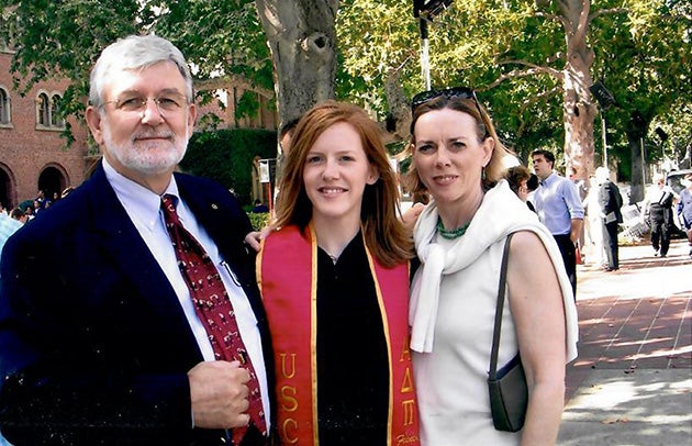 A photo of Kate McCutchen wearing a graduate robe and stole standing between her parents on Trousdale Parkway.