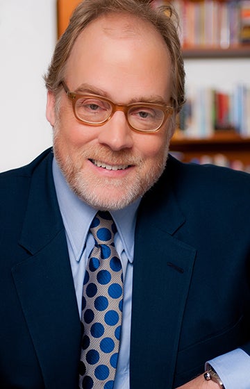 Portrait of Mike Murphy wearing glasses, a dark blue suit coat, a light blue dress shirt and a gray tie with blue dots